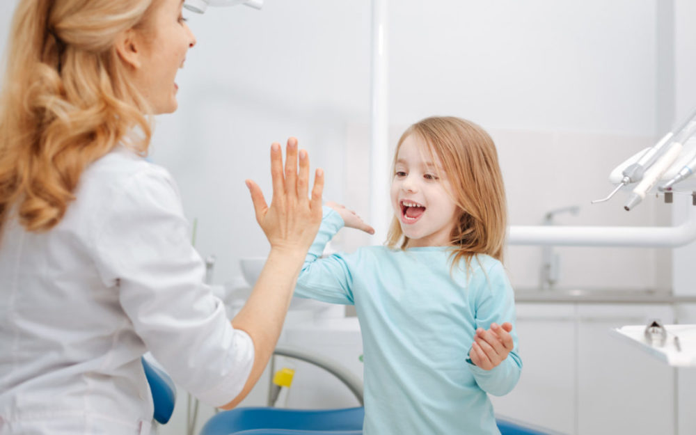 Creative professional dentist giving her little patient a high five